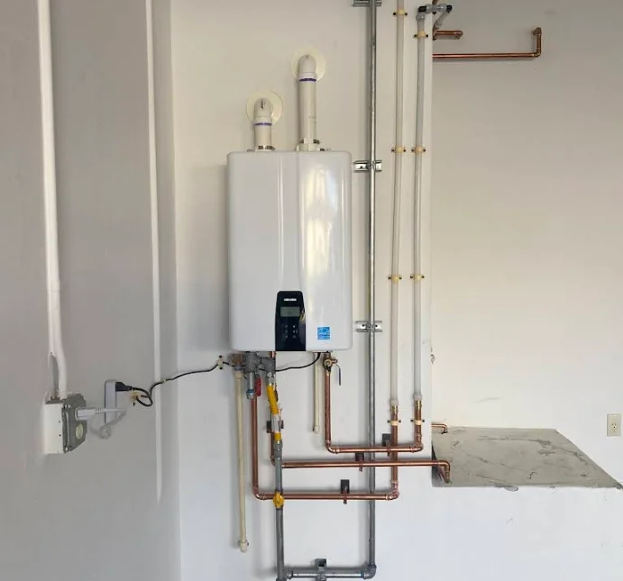White cylindrical electric water heater unit with black control panel and elements, installed in a utility space, featuring brand labeling and plumbing connections, from Copperhead Plumbing services.